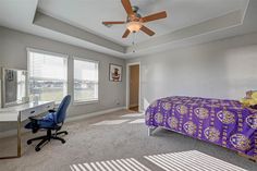 a bedroom with a bed, desk and ceiling fan in the middle of the room