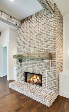 a brick fireplace in the middle of a room with wood flooring and white walls