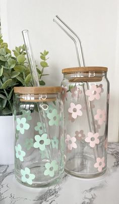 two mason jars with flowers painted on them, one has a straw and the other has a lid