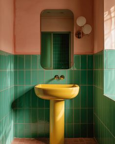 a bathroom with green and pink tiles, a yellow pedestal sink and mirror on the wall