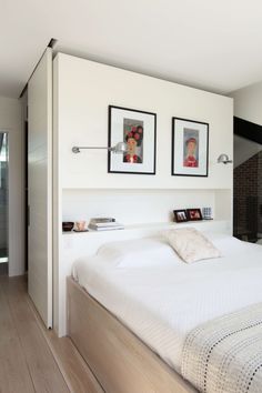 there is a bed with white sheets and pictures on the wall above it in this bedroom