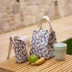 two bags sitting on top of a wooden table next to an apple and a cup