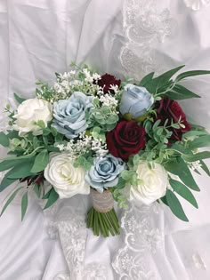 a bridal bouquet with roses and greenery on a white cloth draped in lace