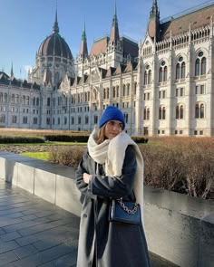 a woman standing in front of a large building wearing a blue beanie and coat