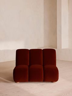 a red couch sitting on top of a hard wood floor next to a white wall