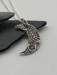 This unique silver moon necklace has been entirely handmade using .999 fine silver. It has been cut from fine silver precious metal clay, textured, fired and oxidized. The pendant hangs from a sterling silver diamond cut cable chain. This fine silver pendant features an embossed paisley print pattern and hangs 1 1/4 from top of ring to bottom of the moon shape. Pendant size: approximately 5/8 x 1/2 inches Chain length: adjustable at 16 and 18 inches can also be customized to whatever length need Handmade Crescent Sterling Silver Jewelry, Bohemian Sterling Silver Moon Phase Necklace, Bohemian Moon Phase Necklace In Sterling Silver, Artisan Silver Necklace With Moon Charm, Artisan Silver Necklace With Moon Phase Detail, Artisan Silver Necklace With Moon Phase, Artisan Silver Jewelry With Moon Charm, Bohemian Silver Necklace With Moon Phase, Nickel Free Half Moon Silver Necklace