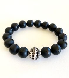 "Matte Tibetan black onyx stretch bracelet with beaded pewter focal bead accent. 10mm grade A Tibetan black onyx gemstones are matte with polished band through the middle. That are all natural stones. Accent is 12mm beaded Greek ball in antique silver pewter. Made in USA. Made to order on stretch elastic. When selecting size please add 3/4\" to 1\" to your actual wrist measurement for a comfortable fit. Black onyx is known as a powerful stone of protection." Black Stretch Bracelet With Polished Beads, Black Spiritual Stretch Bracelet With Polished Beads, Black Gemstone Beads Stretch Bracelet, Black Stretch Bracelet With Gemstone Beads, Black Hand-strung Stretch Bracelet, Black Adjustable Stretch Bracelet With Gemstone Beads, Onyx Gemstone Beads Stretch Bracelet, Spiritual Onyx Stretch Bracelet With Round Beads, Round Onyx Stretch Bracelet With 8mm Beads