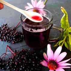 a person holding a spoon over a cup filled with blackberries and elderberry syrup