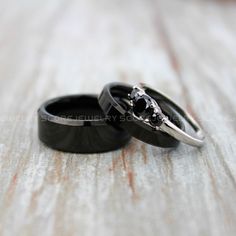 two wedding rings with black diamonds on them sitting on a wooden table, close up