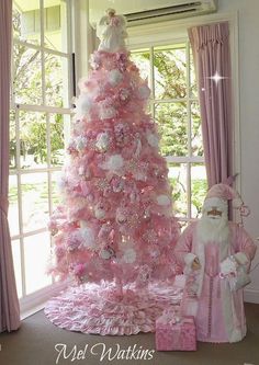 a pink christmas tree decorated with white and pink ornaments is in front of a window