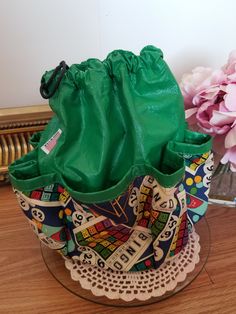 a green bag sitting on top of a wooden table next to flowers and a vase