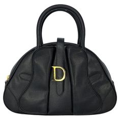 This Christian Dior Double Saddle Bowler Bag was made in Italy and it is finely crafted of a black calfskin leather exterior with gold-tone hardware features such as protective studs at the base and the logo. It has dual rolled leather top handles. It has a slip pocket on the backside. It has a fold over Velcro strap with a zipper closure and it opens up to a black nylon interior with a zipper pocket. It is also certified authentic by Entrupy! Brand: Christian Dior Date/Authenticity Code: MA-002 Wallet Chains, Bowler Bag, Dior Saddle, Dior Vintage, Front Face, Handbag Handles, Wallet Accessories, Saddle Bag, Casual Backpack