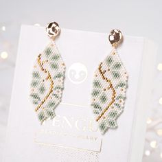 a pair of beaded earrings sitting on top of a white box with lights in the background