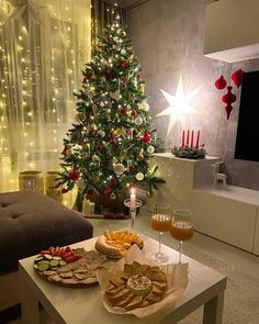 a christmas tree in the living room with food and drinks on the coffee table next to it