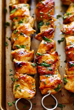 chicken skewers are lined up on a baking sheet with tongs and garnishes