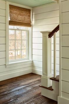 an empty room with wooden floors and white walls, along with a window in the corner