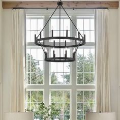 a chandelier hanging over a dining table in front of a window with curtains