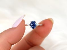 a woman's hand holding an engagement ring with a blue sapphire and diamond band