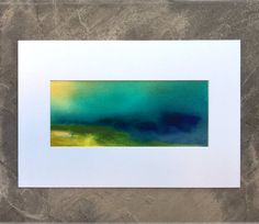 an abstract painting with blue, green and yellow colors on a white frame hanging on a wall