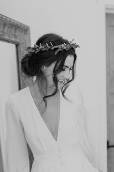 a woman wearing a white dress and a flower crown on her head is looking at herself in the mirror