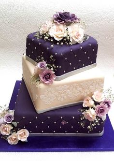 three tiered wedding cake with purple and white flowers on the top, sitting on a blue table cloth