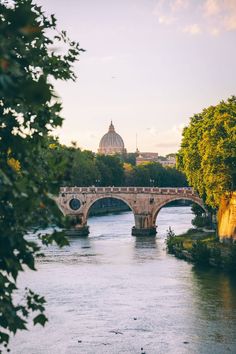 a bridge over a river with a domed building in the background and trees on both sides