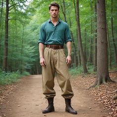 a man standing on a dirt road in the middle of a forest wearing brown pants and green shirt