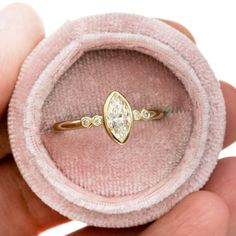 a person holding a ring with a diamond on it's side in a pink velvet case