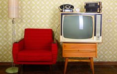 an old fashioned television sitting on top of a wooden dresser next to a red chair