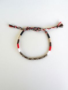 a red, white and black cord bracelet with tassels on a white surface