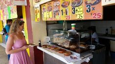 a woman standing in front of a food stand holding a plate with donuts on it