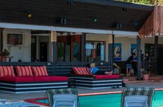 an outdoor pool with lounge chairs and tables next to it, in front of a house