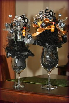 two wine glasses are decorated with black and silver decorations on top of each glass, which is filled with liquor bottles