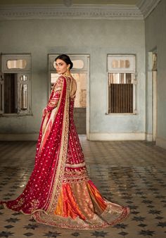 a woman in a red and gold bridal gown standing on a tiled floor with her back turned to the camera