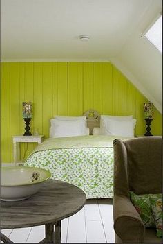 a bedroom with green walls and white bedding in the corner, next to a small round table