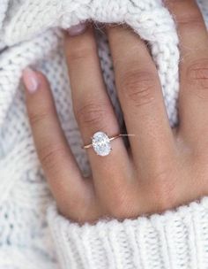 a woman's hand wearing a white sweater and a diamond ring on her finger