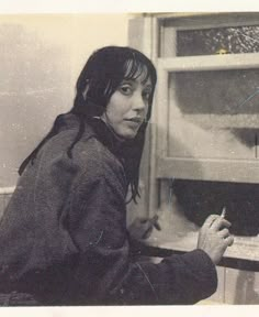 a woman sitting in front of a window writing on a piece of paper