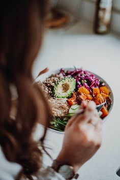 a woman is eating a salad with avocado and carrots on the side