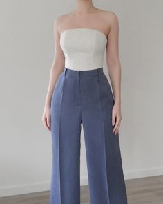 a woman standing in front of a white wall wearing blue pants and a strapless top