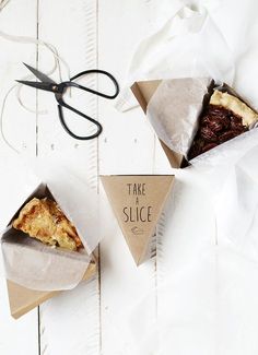 two pieces of food in paper on top of a white wooden table next to scissors