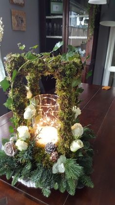 an arrangement of flowers and greenery on a table with a lit candle in the center