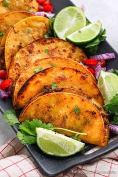 some tacos and limes on a plate with red onion, peppers and cilantro