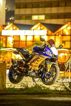 a blue and yellow motorcycle parked in front of a building at night with the lights on