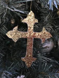 a cross ornament hanging from a christmas tree