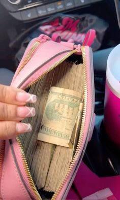 a pink purse filled with money sitting on top of a car dashboard next to a cup