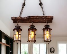 three lights hanging from a wooden beam in a living room with white walls and windows