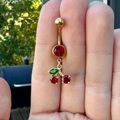 a person is holding up a gold navel ring with red and green jewels on it