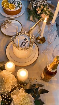 there is a cake on the table with candles and flowers next to some wine glasses