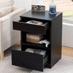 a black night stand with two drawers and a clock on the top one drawer is open