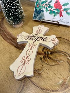 a wooden cross sitting on top of a table next to a christmas tree and greeting card